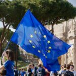a young girl holding a european flag in front of a crowd of people